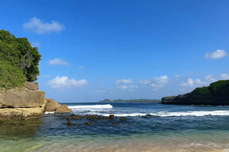 Pemandangan Pantai Tanjung Penyu dengan air laut jernihm langit biru cerah, tebing karang, dan ombak yang tenang di Malang Selatan
