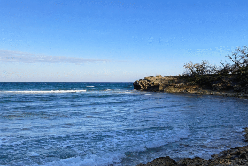 Pemandangan Pantai Kahuripan Gili Genting dengan garis pantai berbatu, tebing alami, dan langit biru terbuka.
