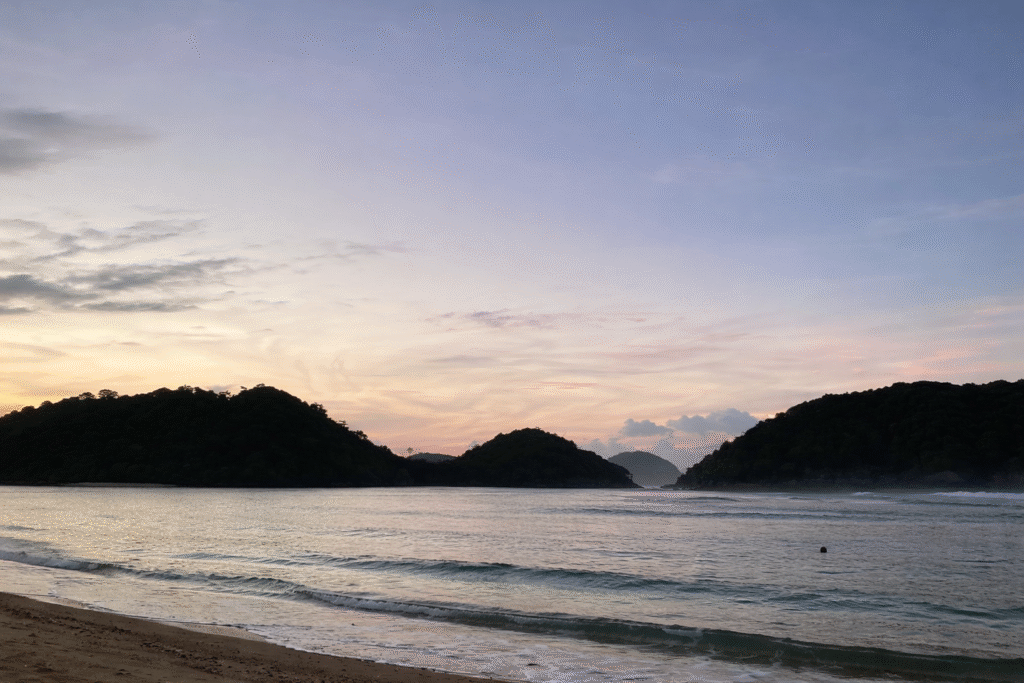 Gerak-gerik Teluk Asmara dengan tebing hijau, dan ombak kecil di sore hari.