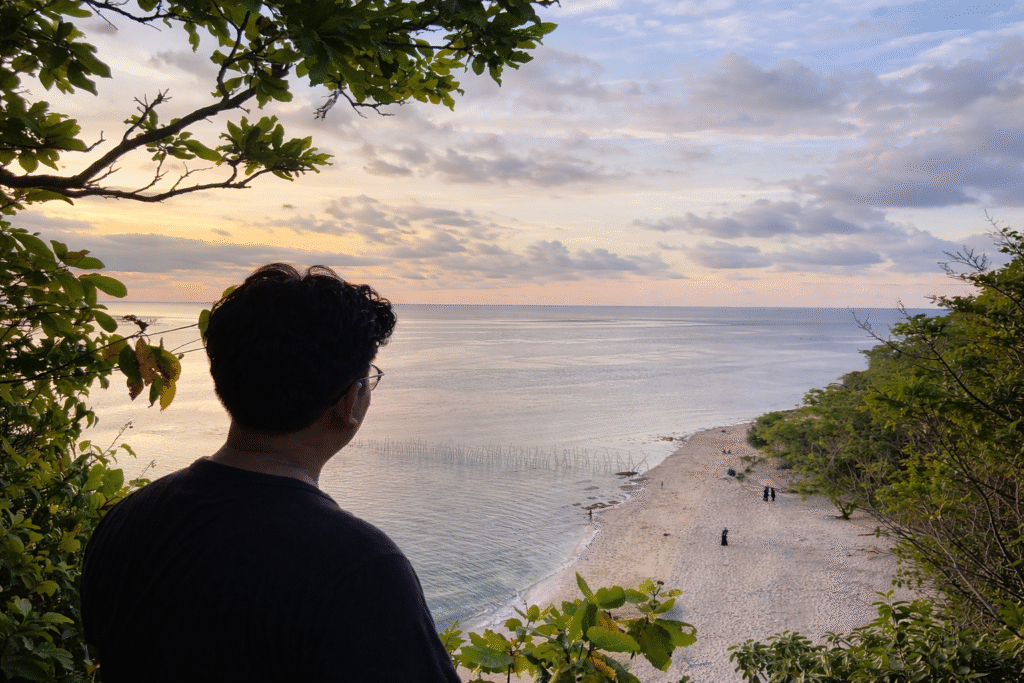 Seseorang memandang Pantai Pasir Putih Kangean dari ketinggian.